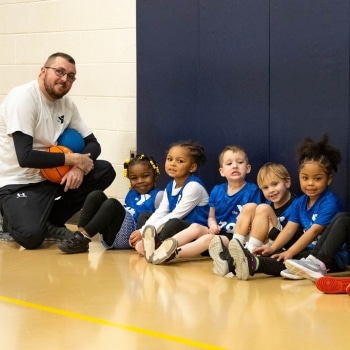 a group of children sitting on the floor with a man and a basketball