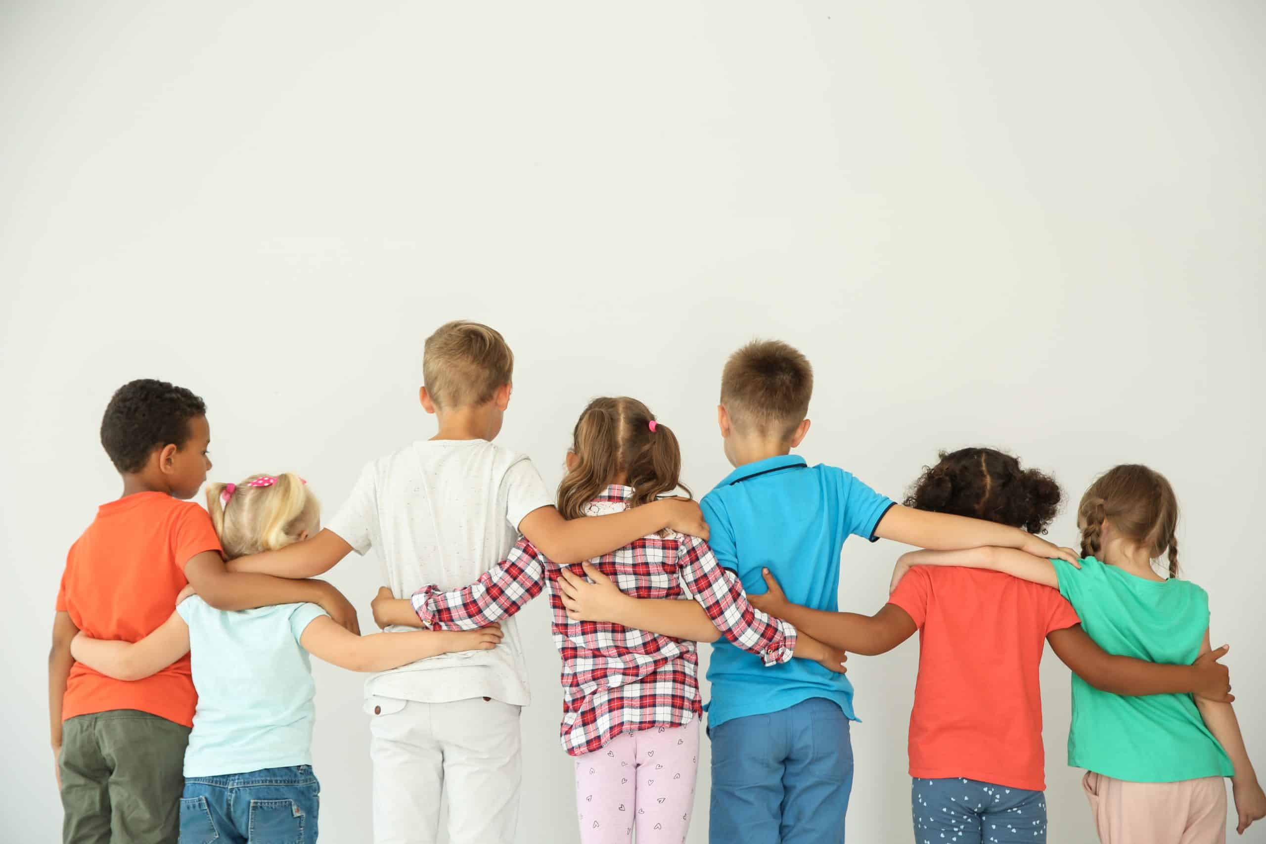 Little children hugging each other with hands on light background.